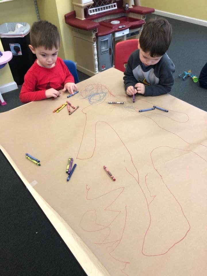 Two children drawing on a large piece of paper with crayons