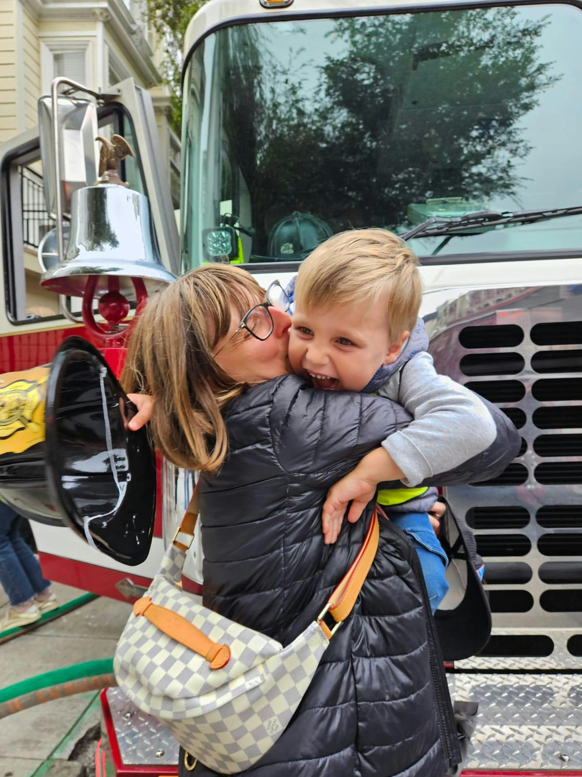 Person kissing a child on the cheek in front of a fire truck