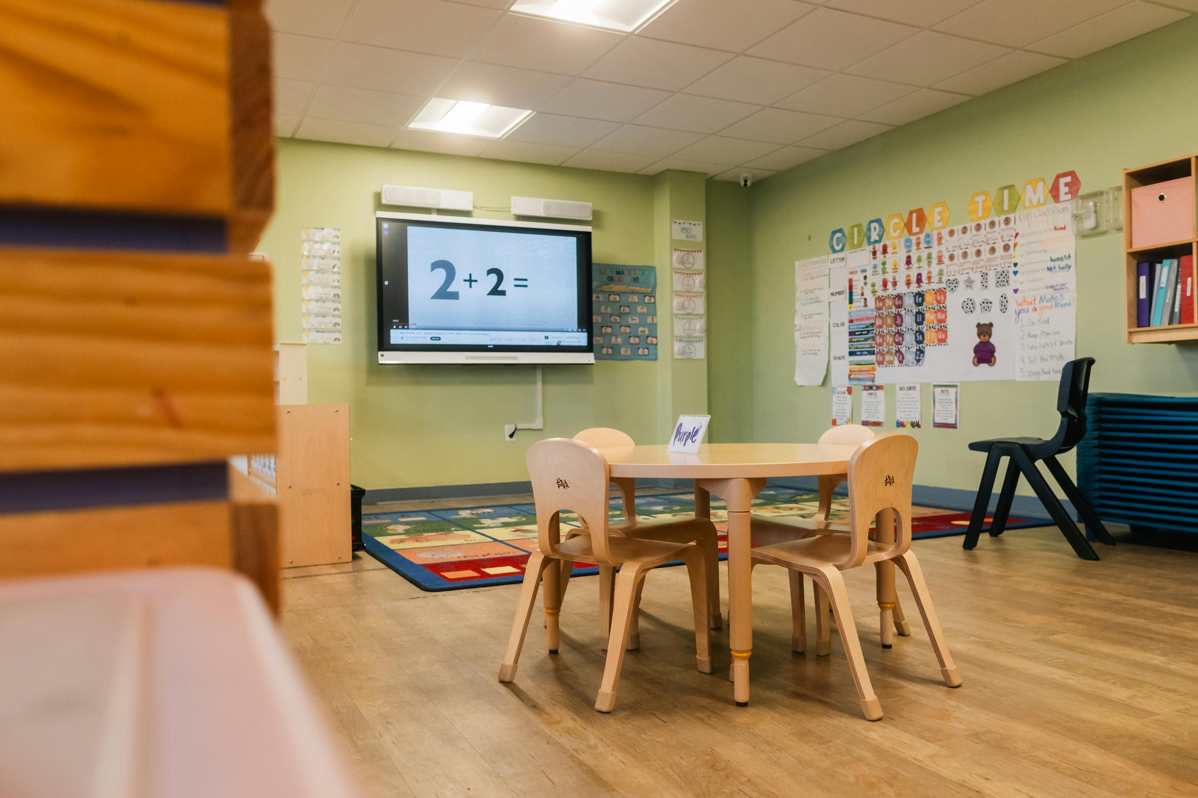 Classroom with small round table and chairs, interactive screen showing "2+2="