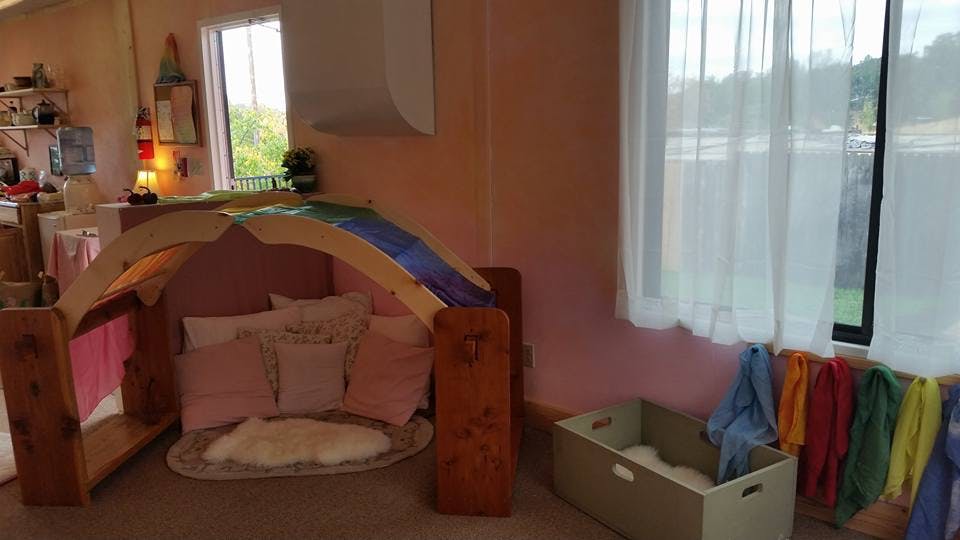 Indoor play area with a wooden arch structure over cushions and a rug