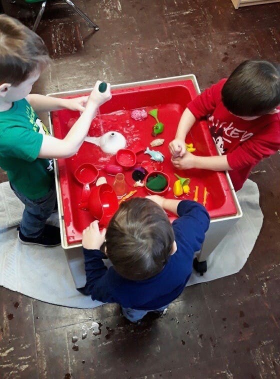Three children playing with toys in a red water table