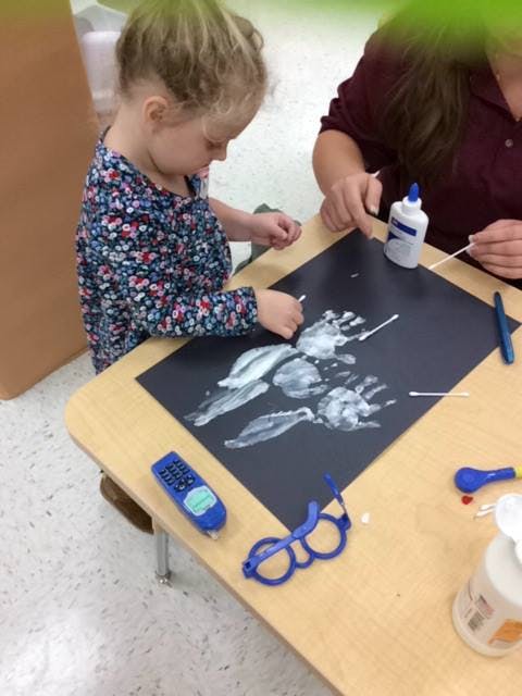 Child and person making handprint art with white paint on black paper