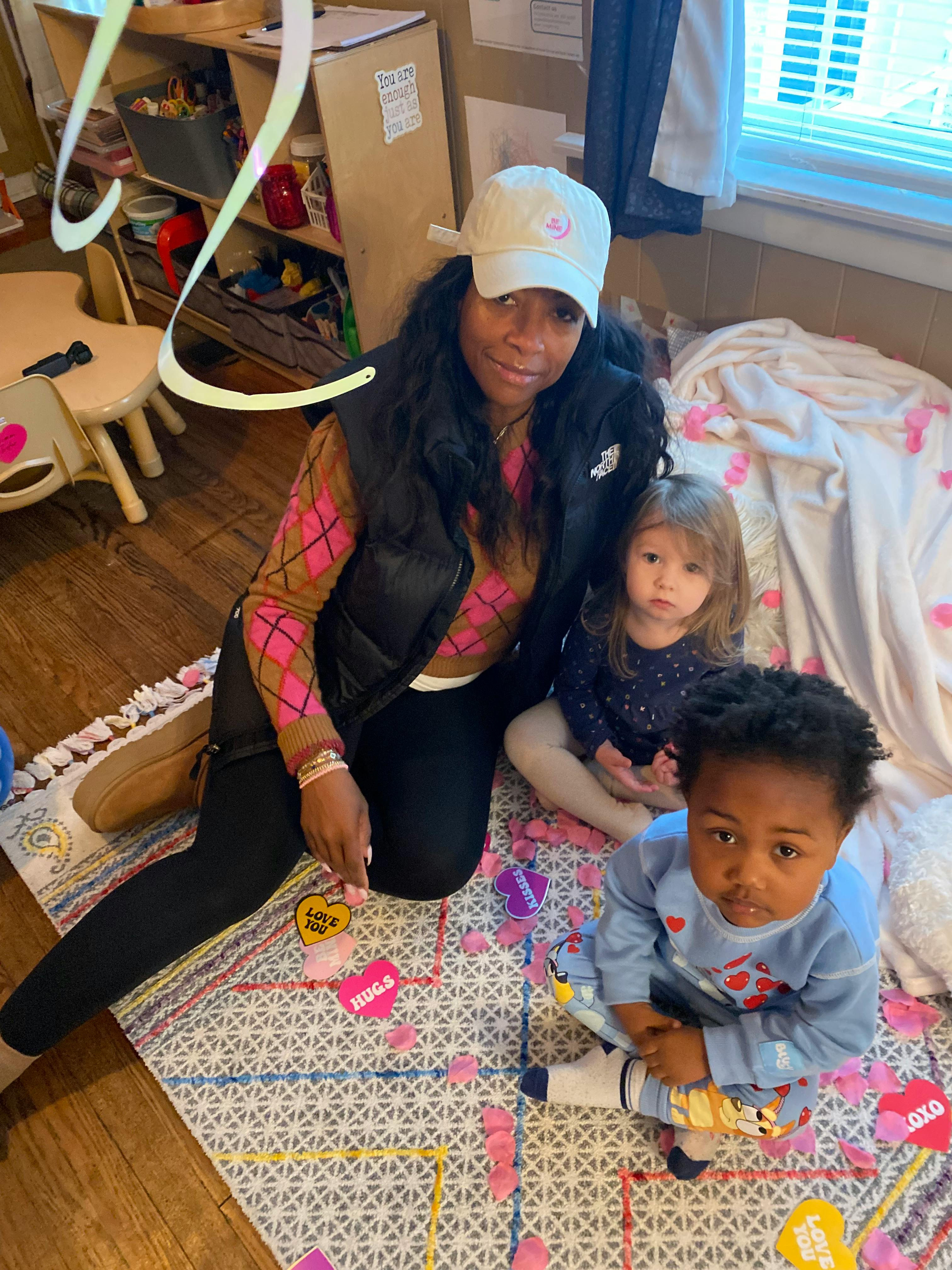 person in a white cap sitting with two children, surrounded by paper hearts