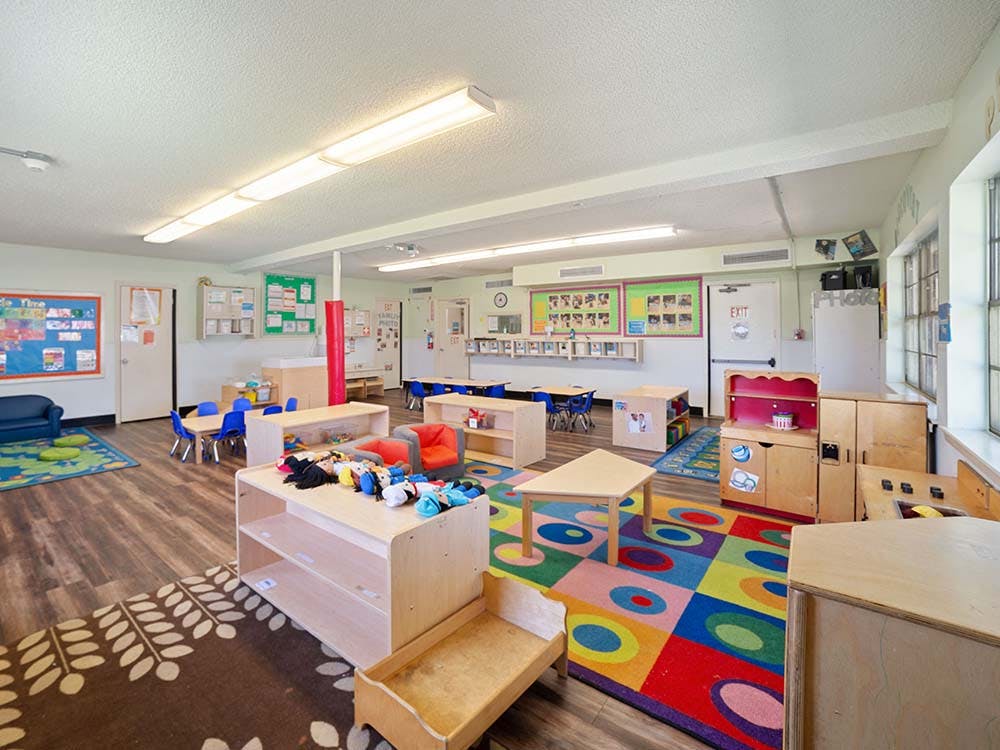 A colorful classroom with small tables, chairs, and play furniture