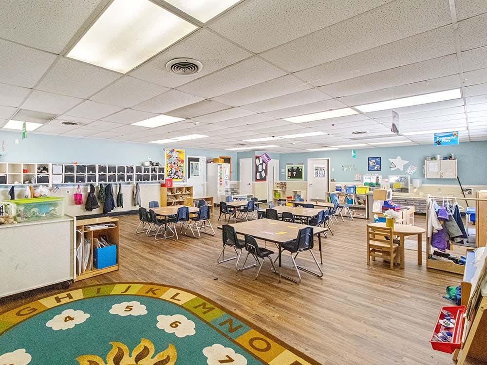 Classroom with small tables and chairs, shelves, and a colorful rug