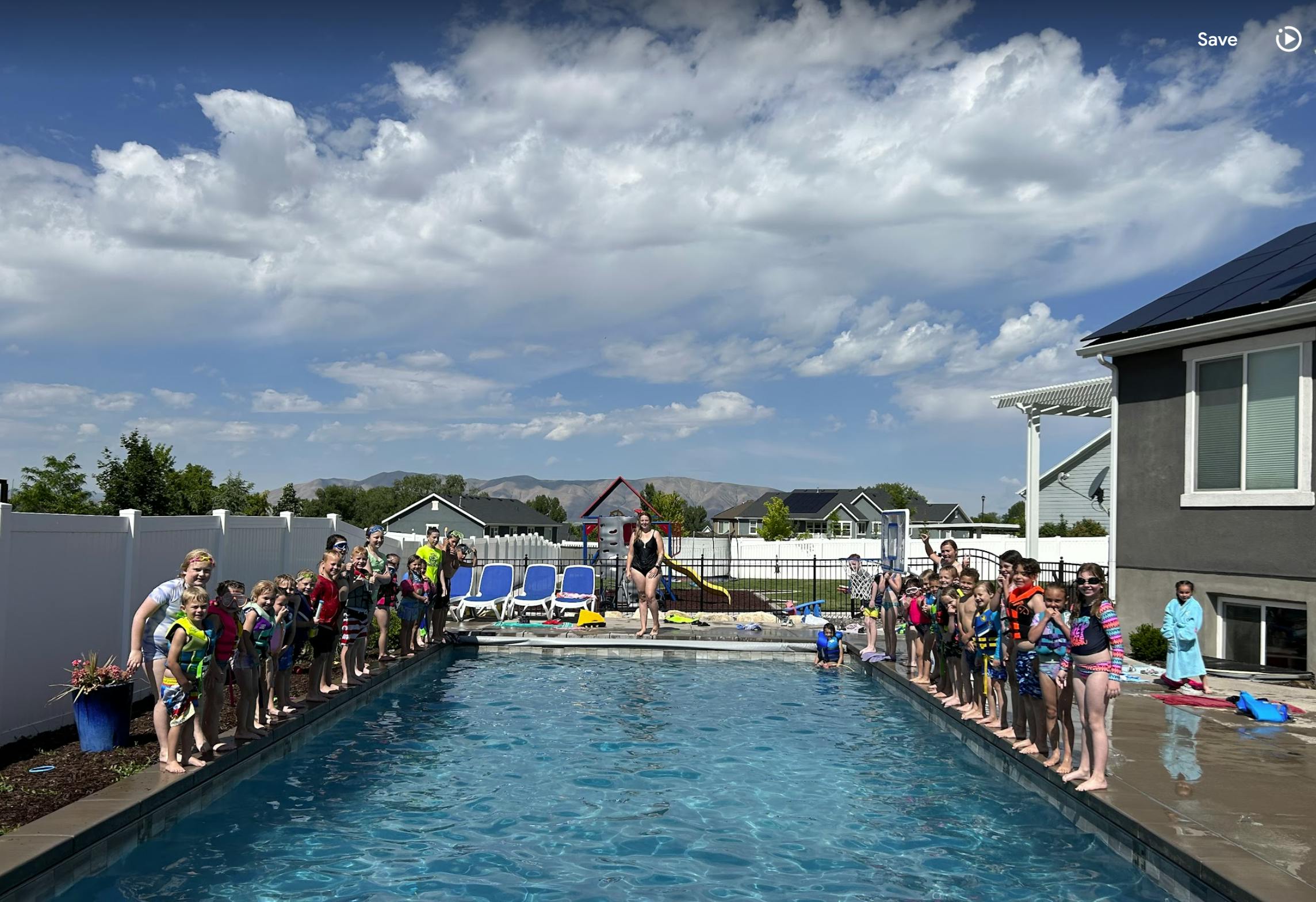 Many children and adults standing on both sides of a swimming pool