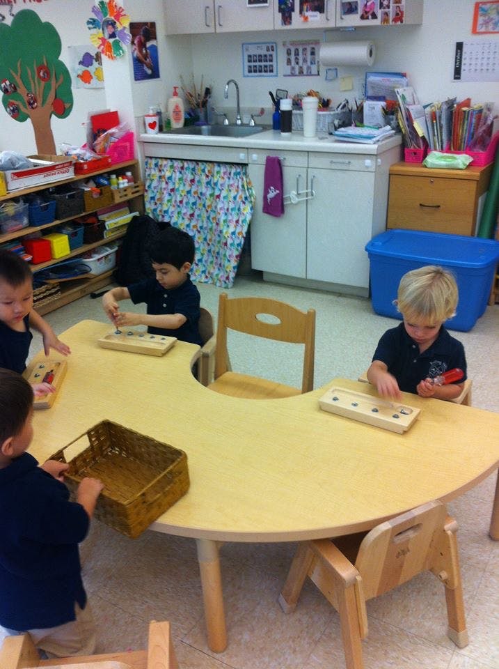 Three children playing with toys at a crescent-shaped table in a classroom
