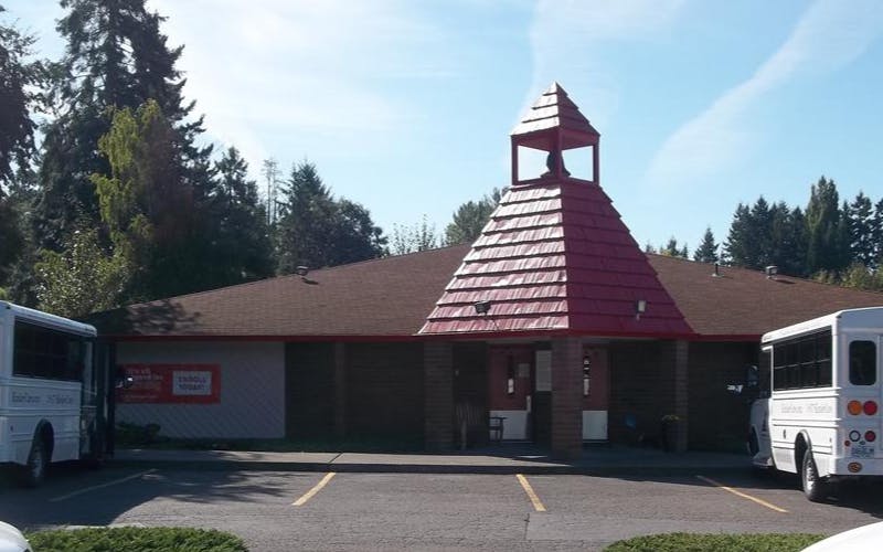building with a red bell tower and two white buses in a parking lot