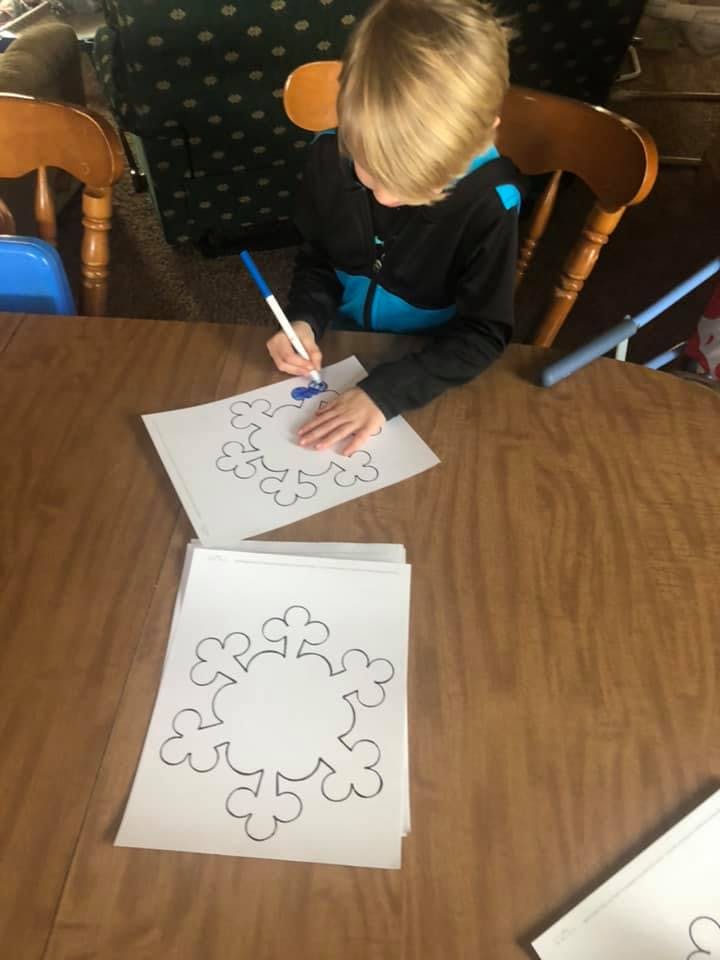 Child coloring a snowflake drawing with a blue marker