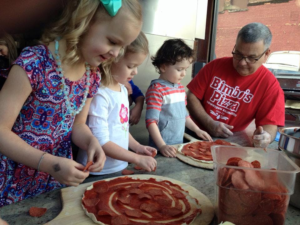 Adult and three children making pizzas, topping pizzas