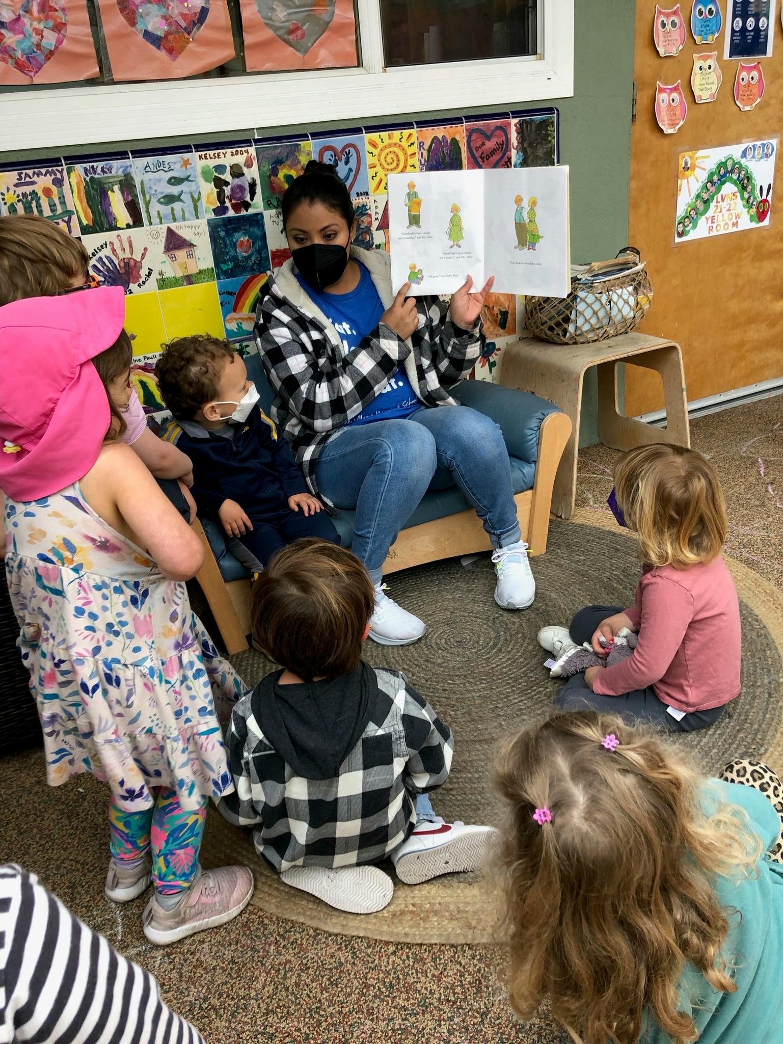 Person in mask reading a book to children in a classroom