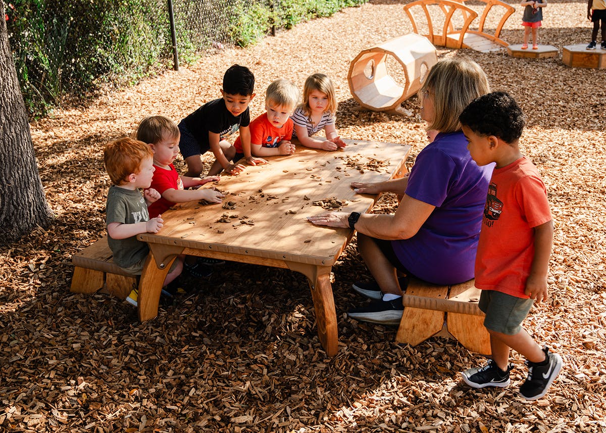 Adult and children gathered around a small wooden table outdoors