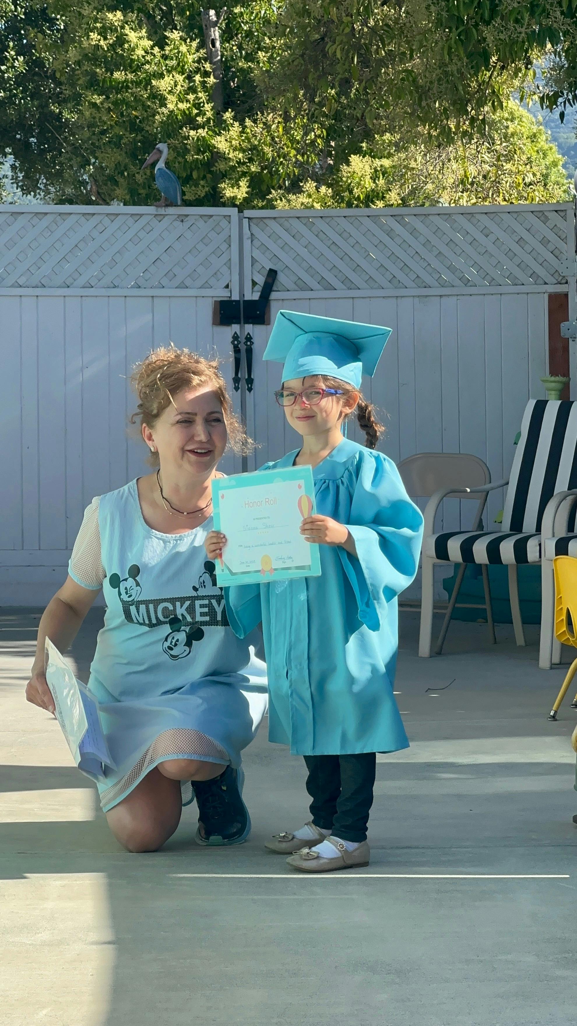 Person kneeling next to a child in a graduation cap and gown holding a certificate