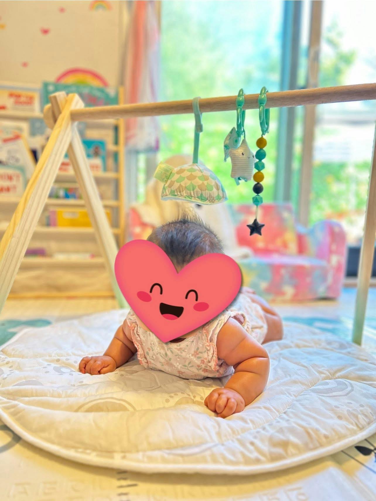 Child on stomach under a wooden play gym with hanging toys