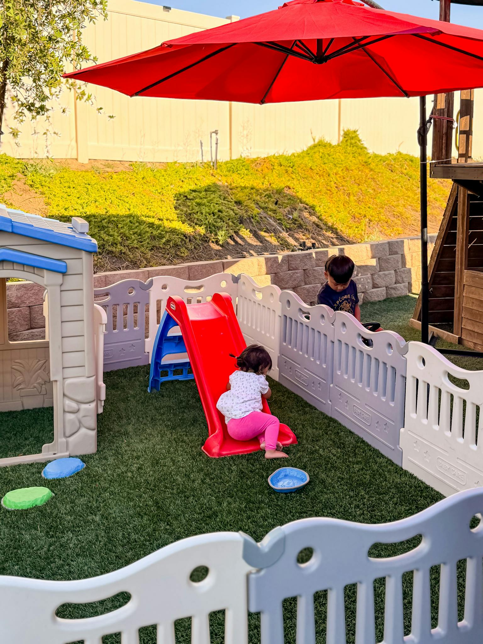 Children playing in a fenced outdoor play area with a plastic slide