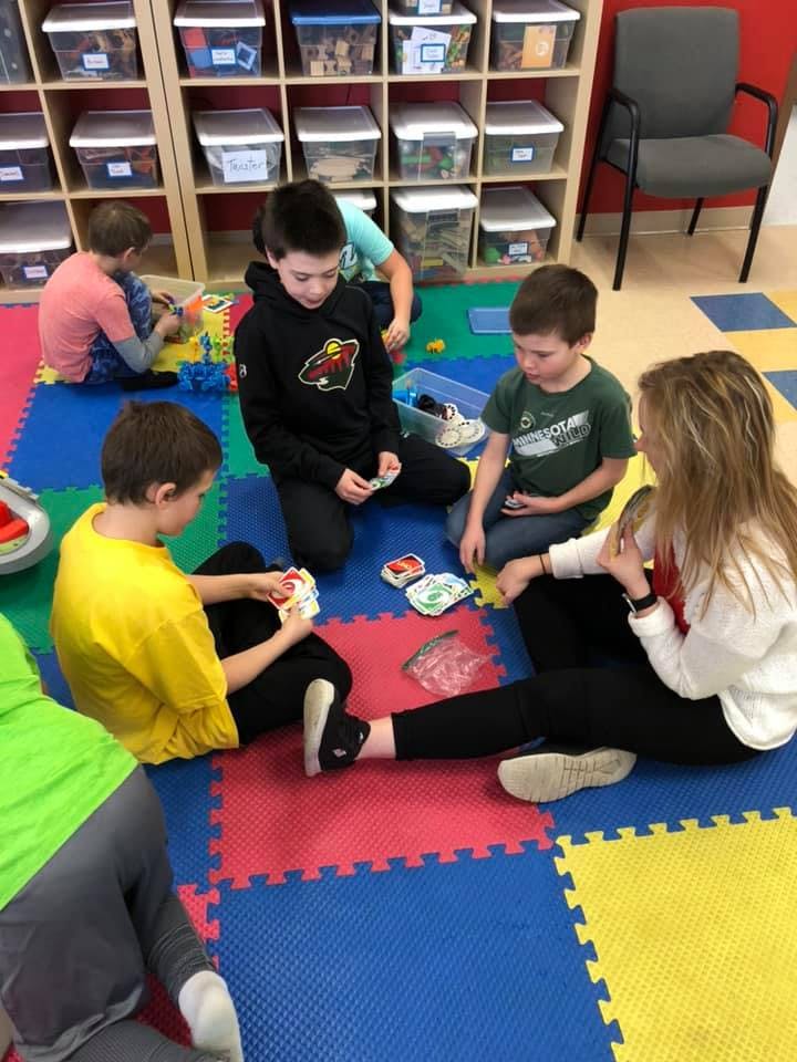 Four children and one adult sitting on a colorful mat playing a card game
