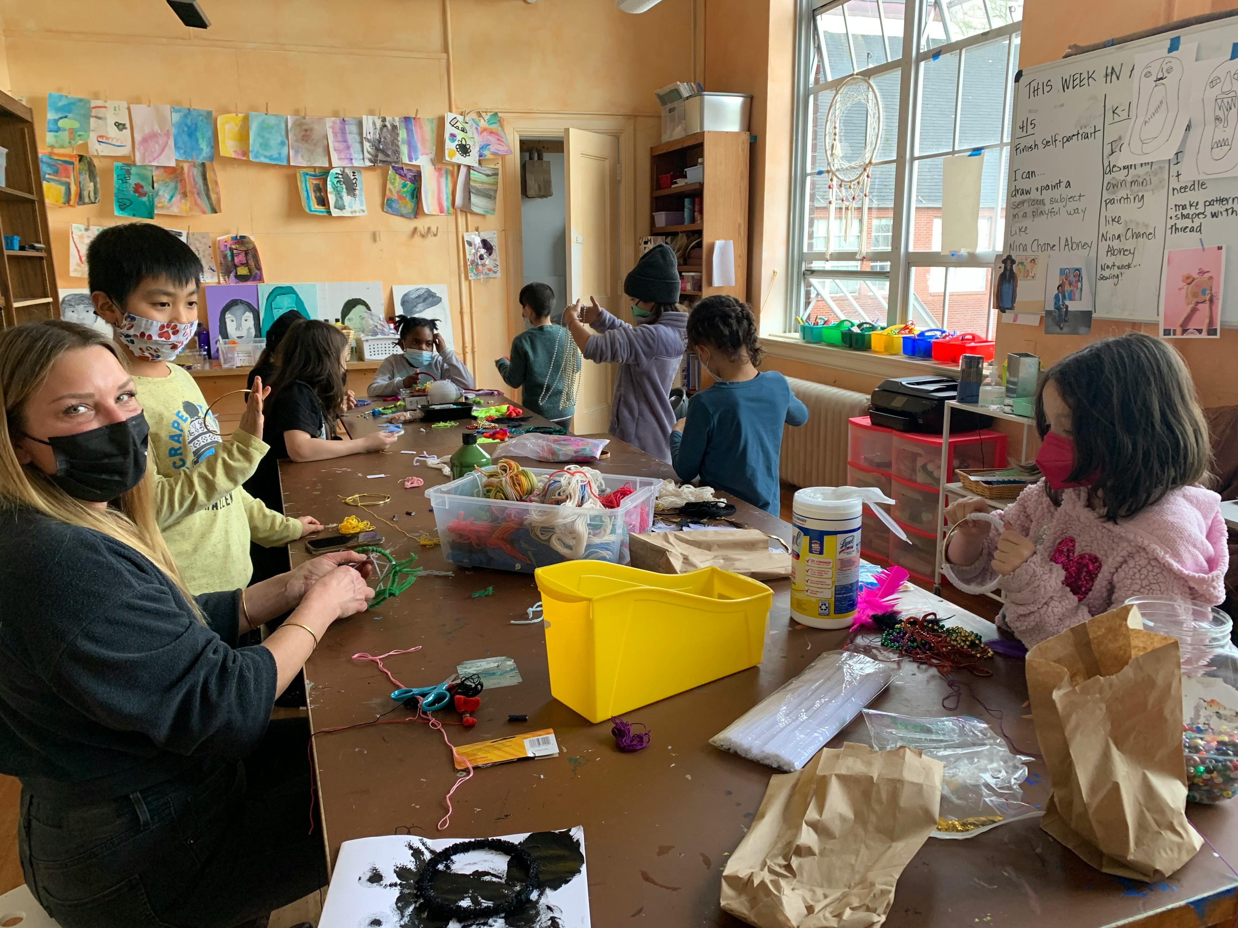 Adult and children working on crafts at a long table in a classroom