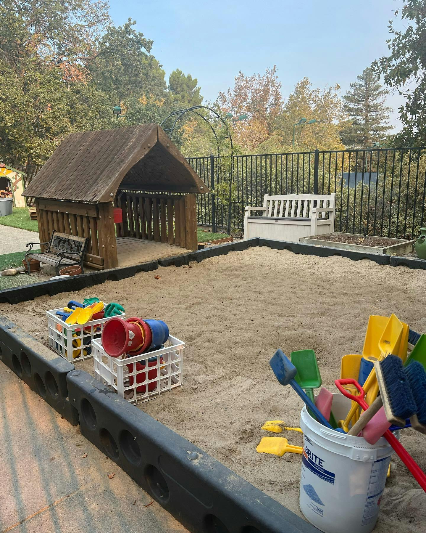 Sandbox with a wooden playhouse and colorful sand toys