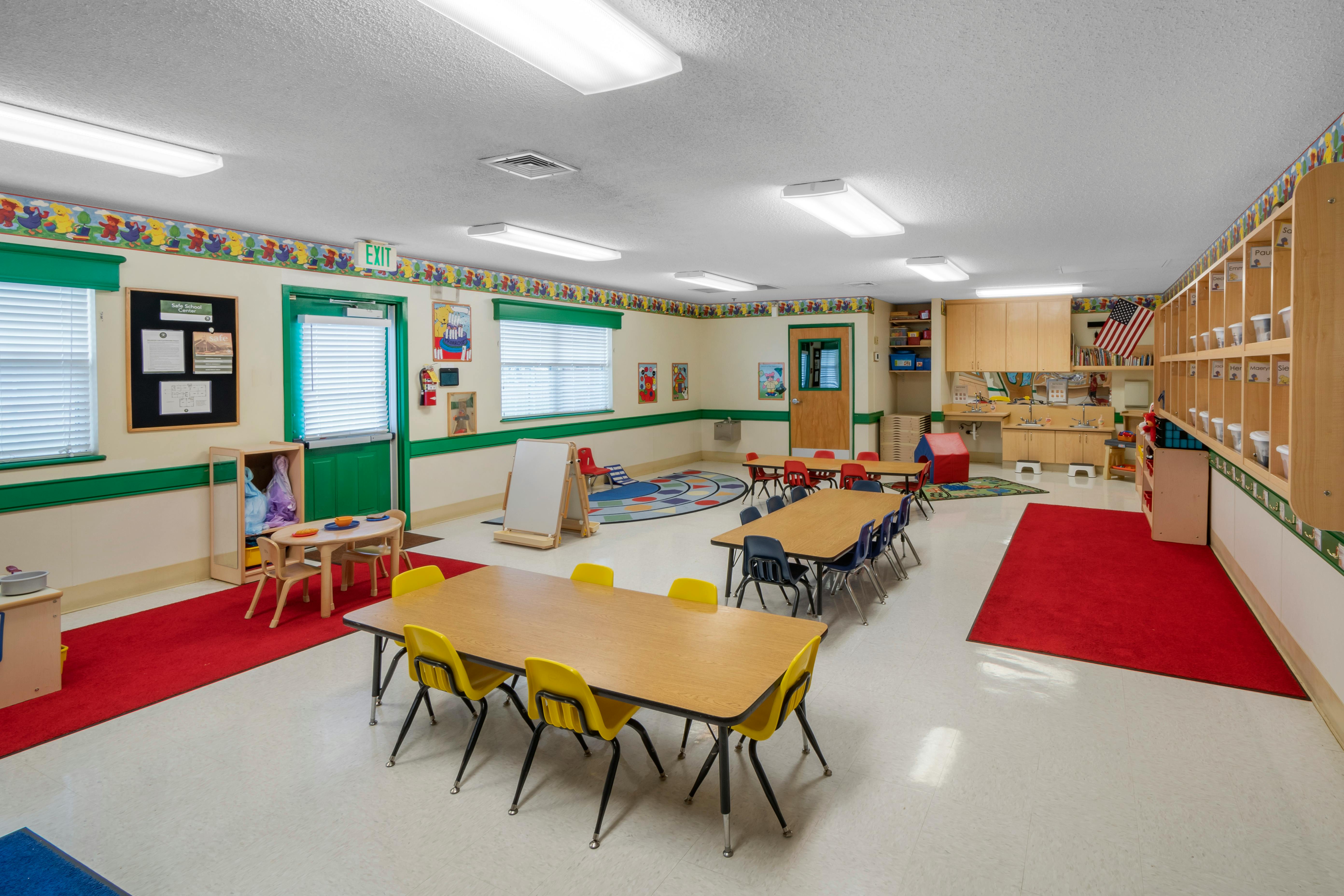 An empty children's classroom with several tables and chairs, and play areas