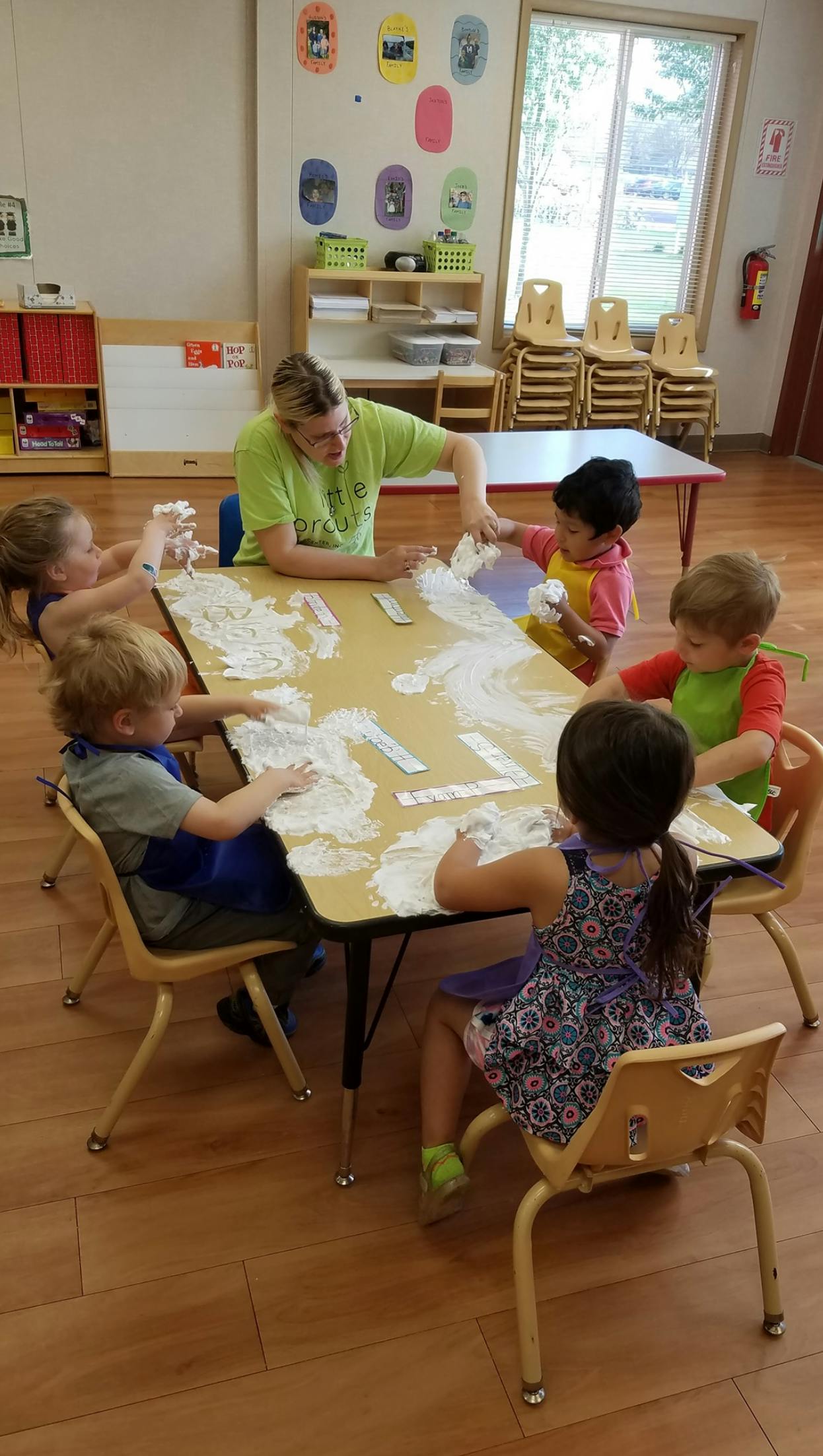 Adult and children playing with shaving cream at a table in a classroom