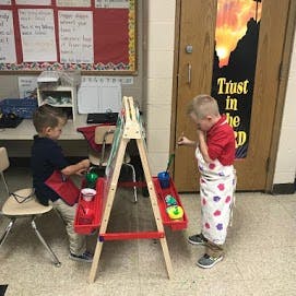 Two children painting at an easel in a classroom