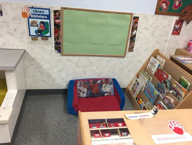 Classroom corner with a red and blue child's chair, book display, and green board