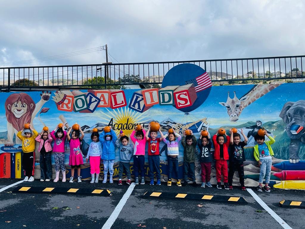 Group of children holding pumpkins on their heads in front of a mural