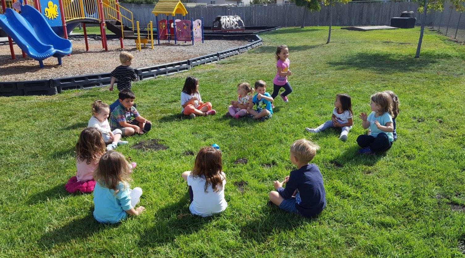 Children sitting in a circle on grass in a playground