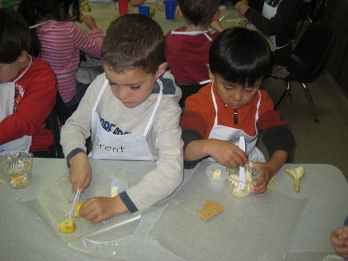 Two children in aprons cutting and mixing food at a table