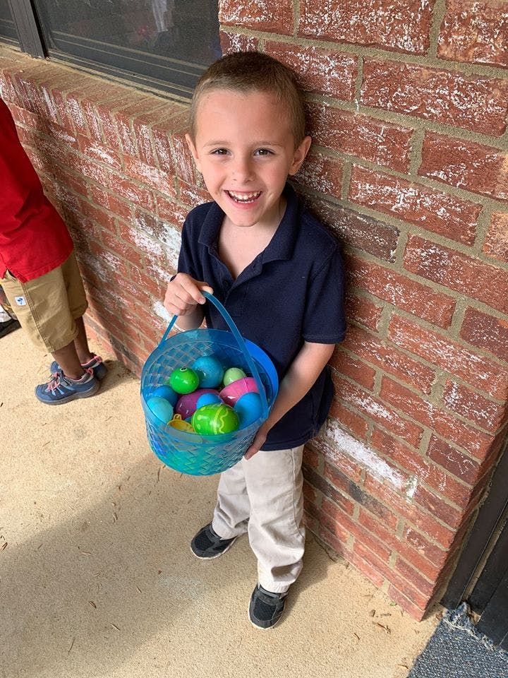 Child holding a blue basket filled with colorful plastic eggs