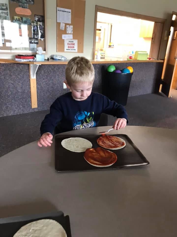 Child spreading sauce on flatbreads on a baking sheet