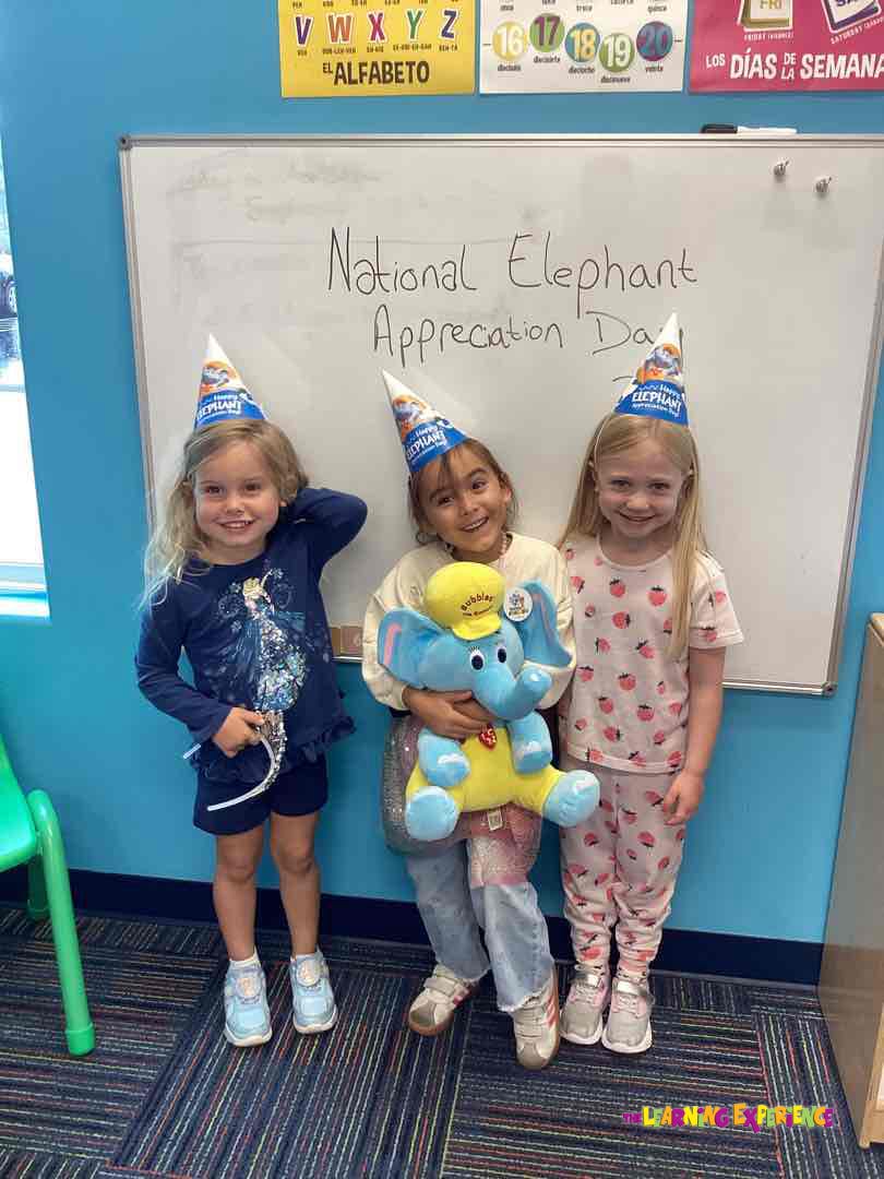 Three children wearing party hats in front of a whiteboard