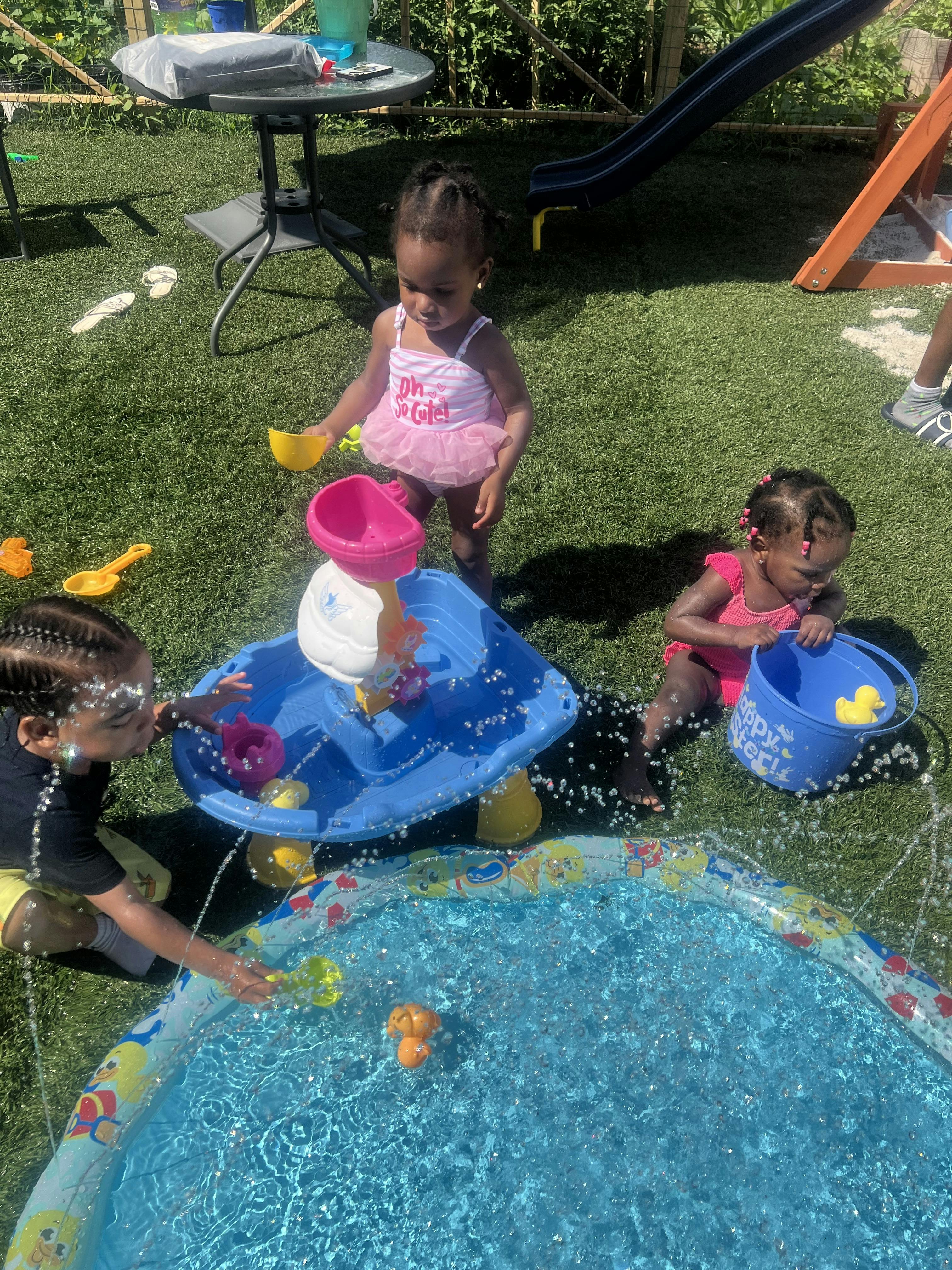 Three children playing with water toys in a backyard on artificial turf