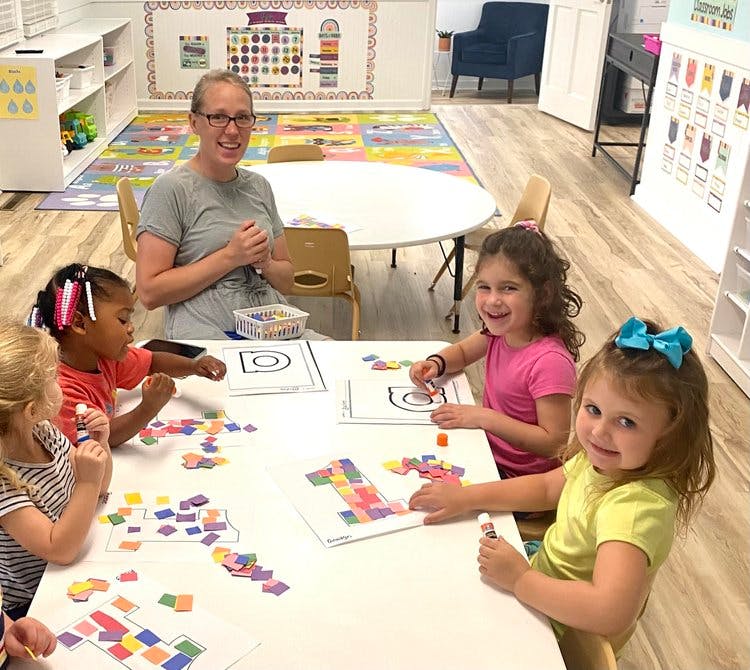 Person and children doing crafts at a table in a classroom