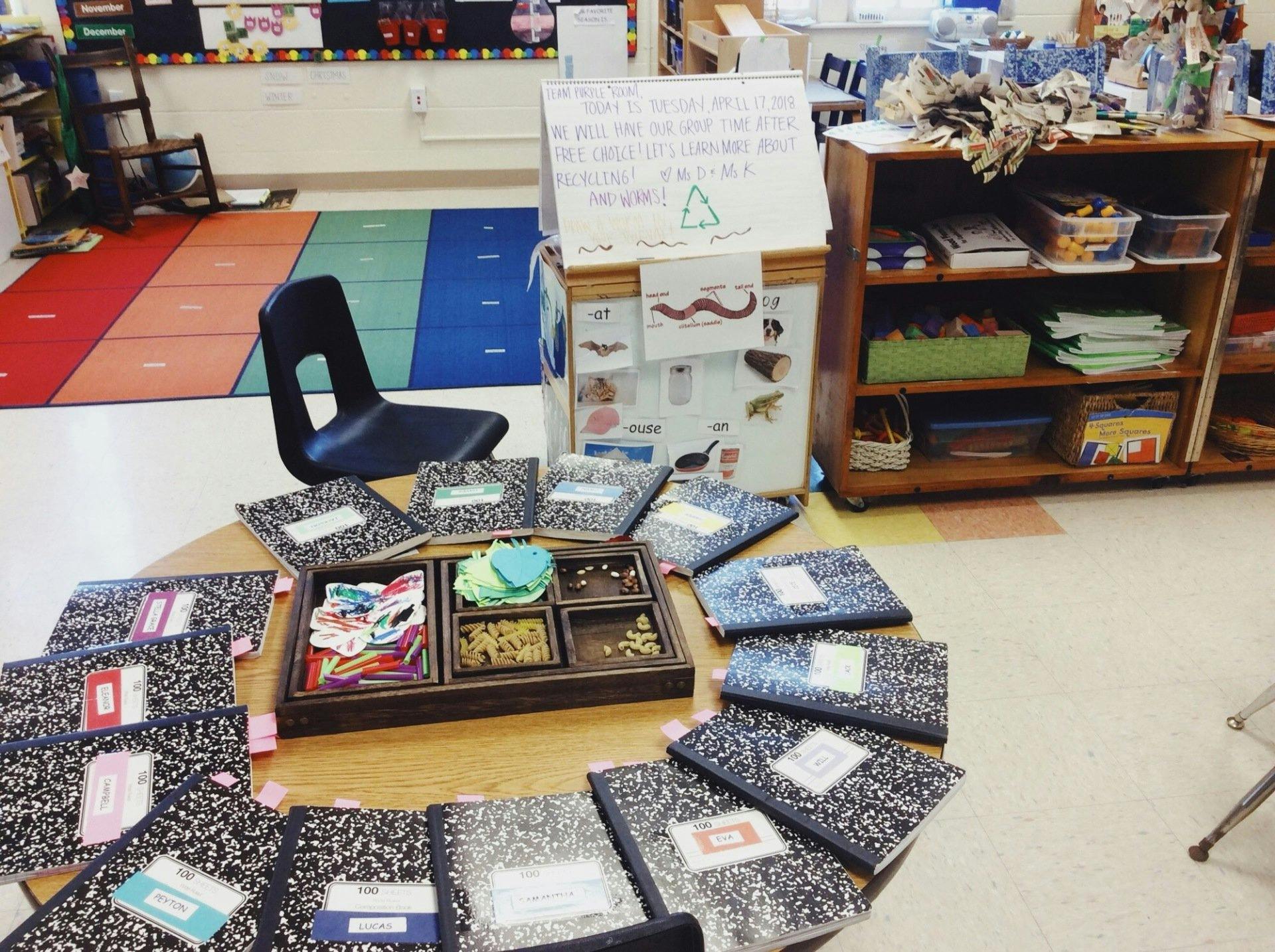 Classroom table with notebooks and a wooden tray of craft supplies