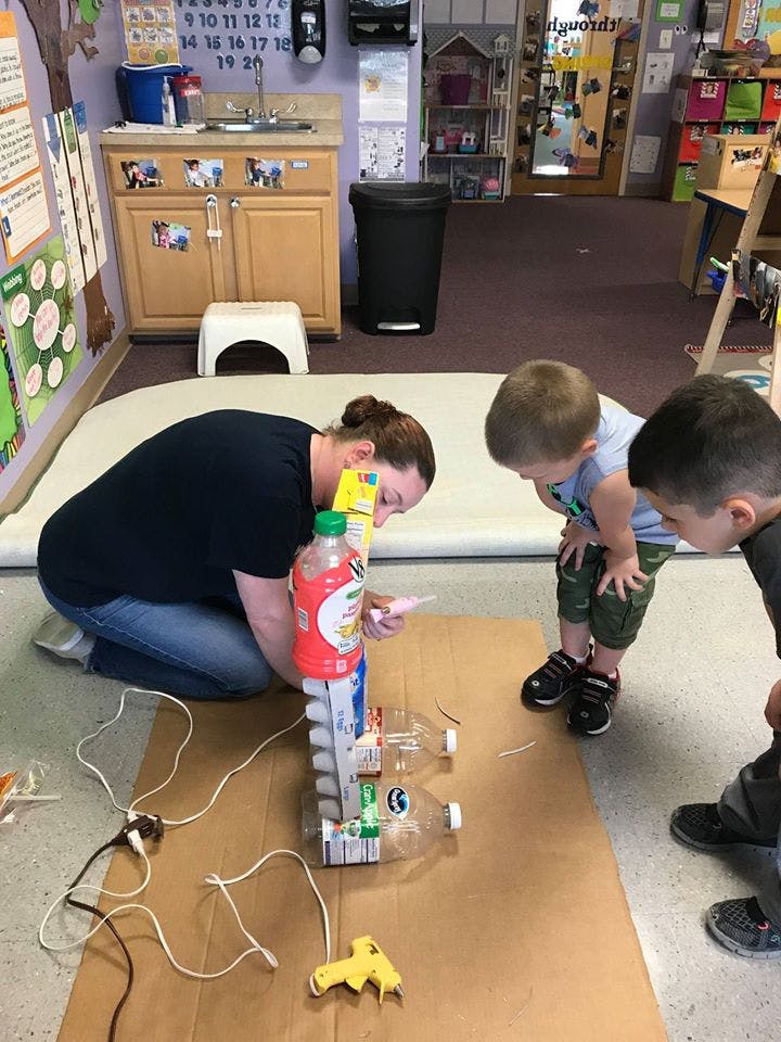 Person and two children building a structure from recycled materials