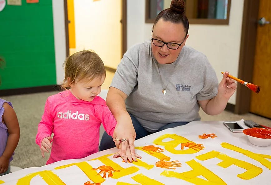 Person helping a child with handprint art