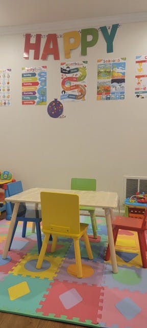 Classroom with a table and chairs on a colorful mat, "HAPPY" banner on wall