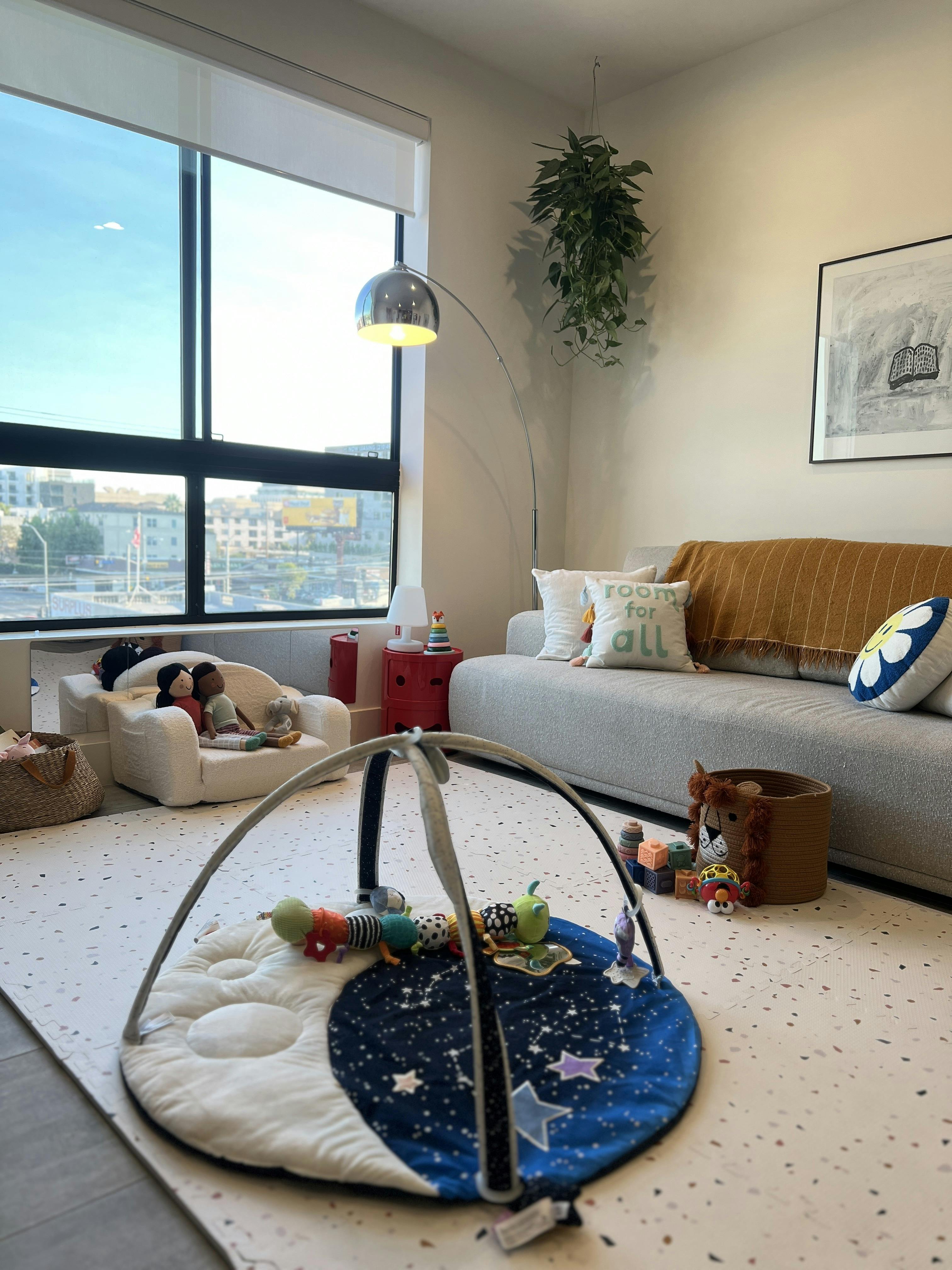 Playmat with toys in a living room with a sofa and large window