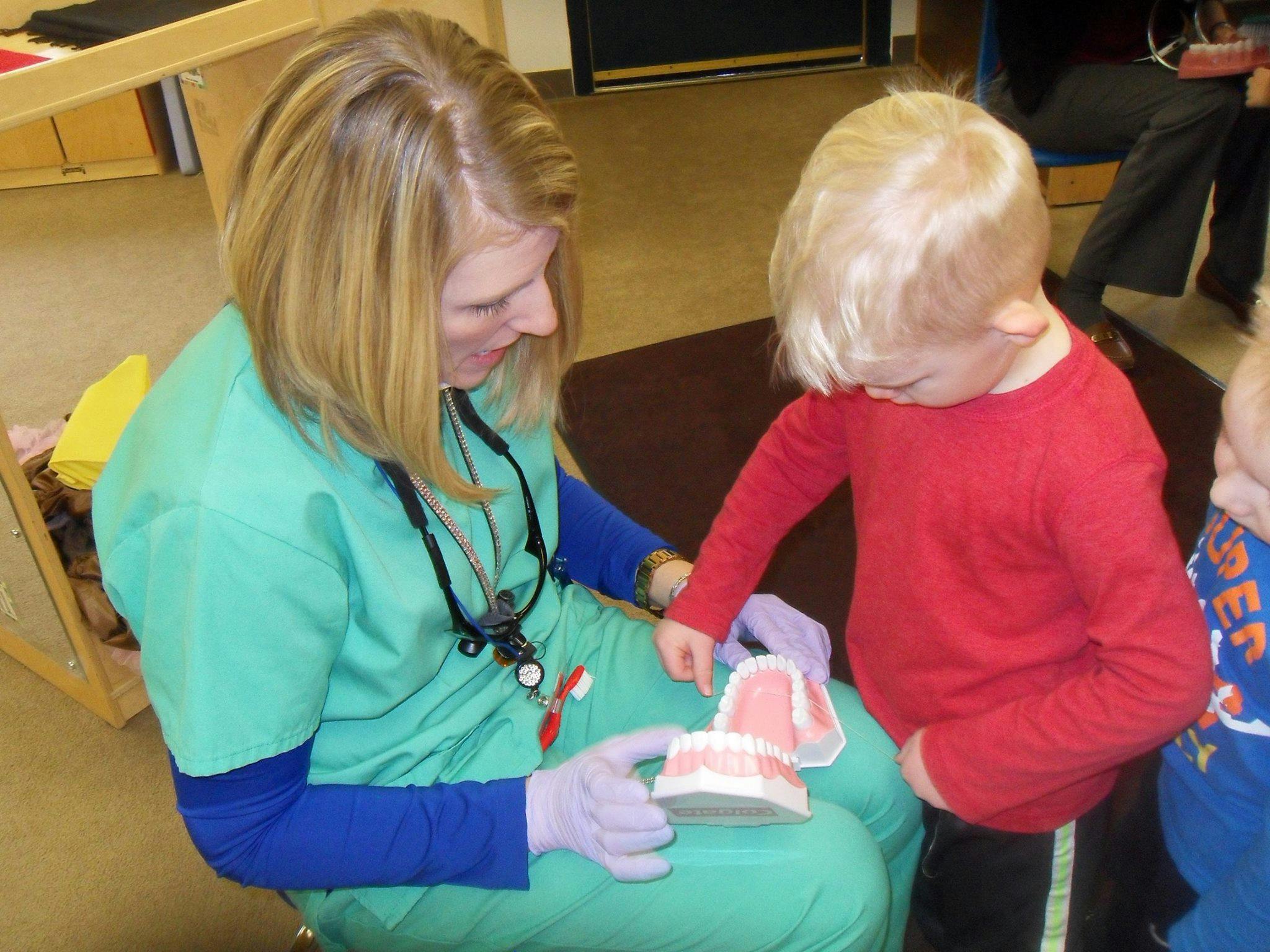 Person in scrubs showing a child a dental model