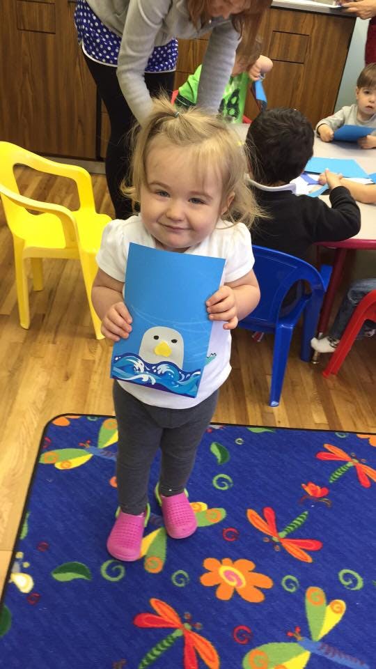 Child holding up a blue paper with a drawing of a bird in waves
