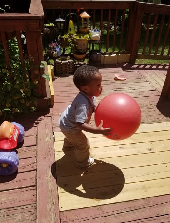 Child holding a large red ball on a wooden deck