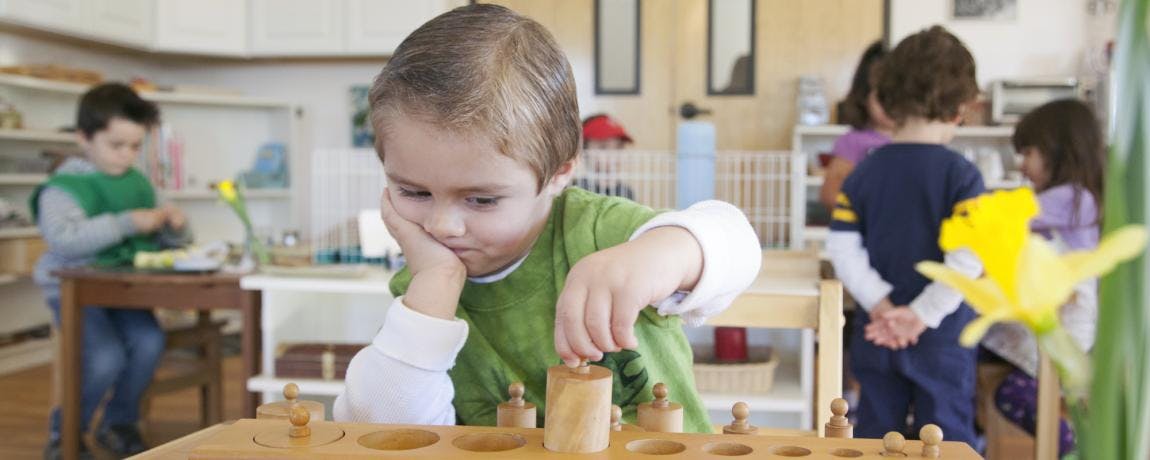 Child playing with wooden blocks at a table in a classroom