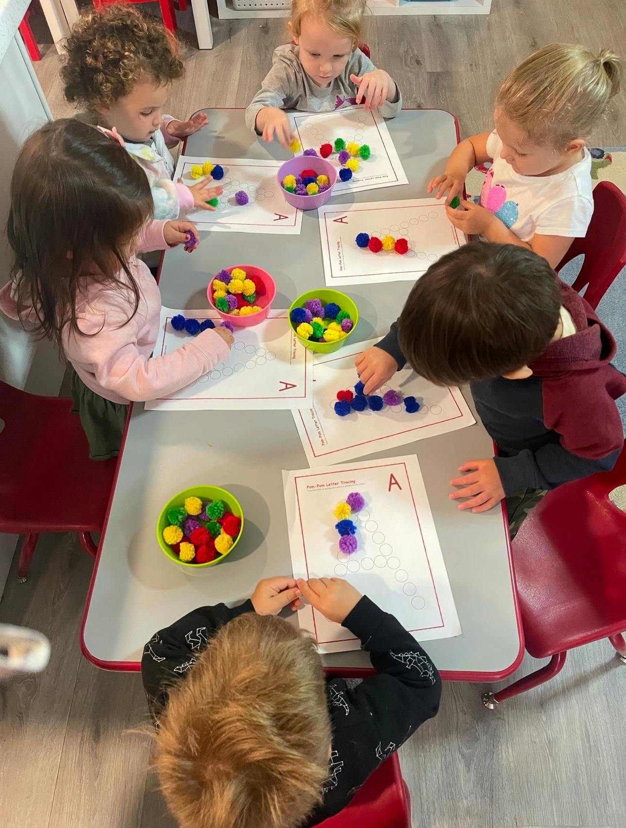 Children at a table playing with colorful pom-poms