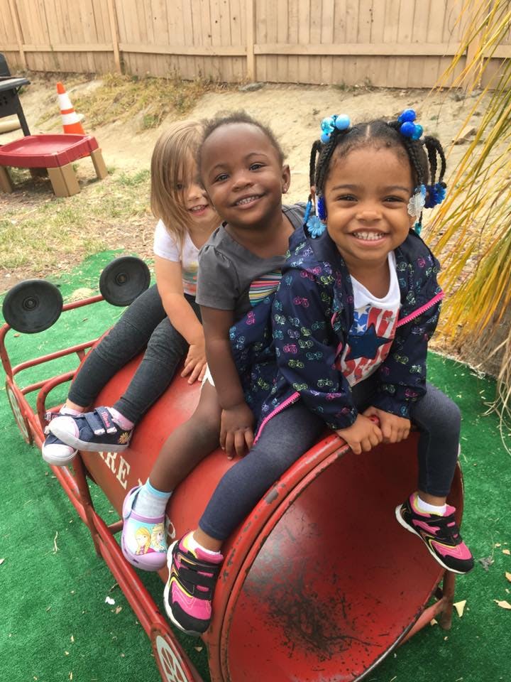 Three children sitting on a red toy car