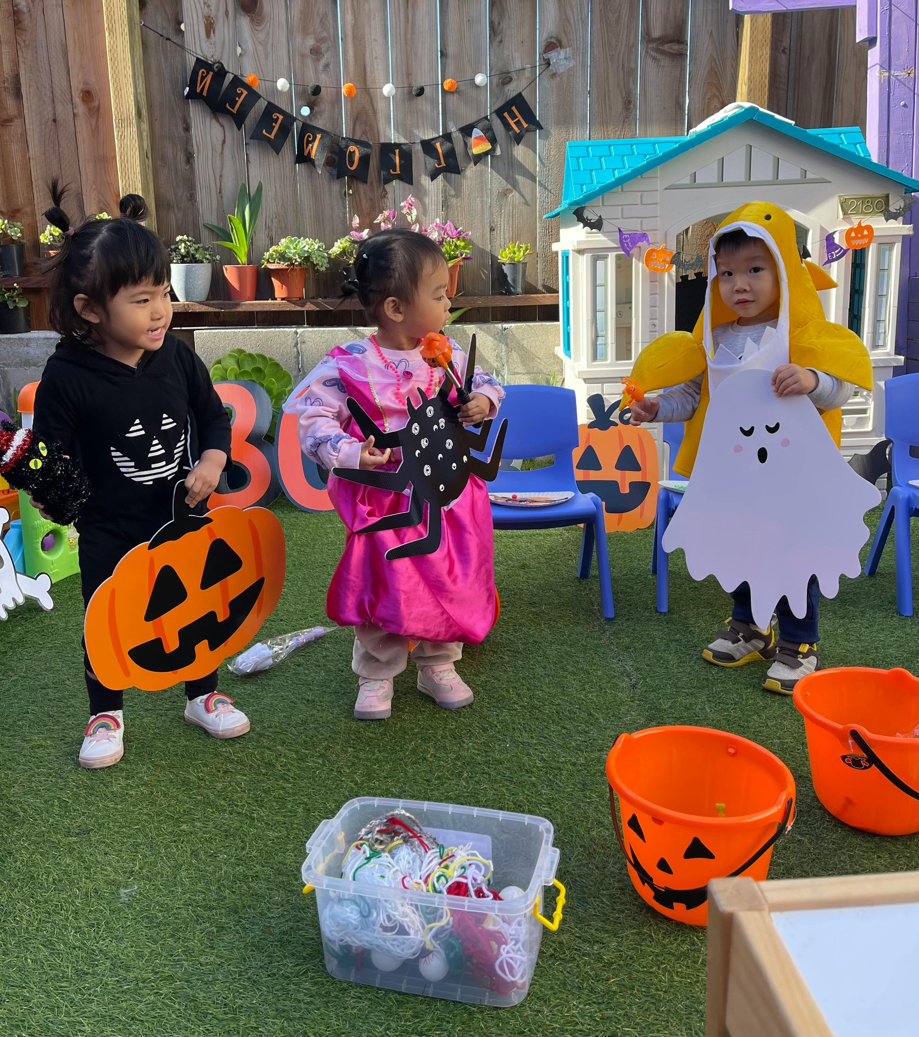 Three children in Halloween costumes holding decorations and wearing decorations