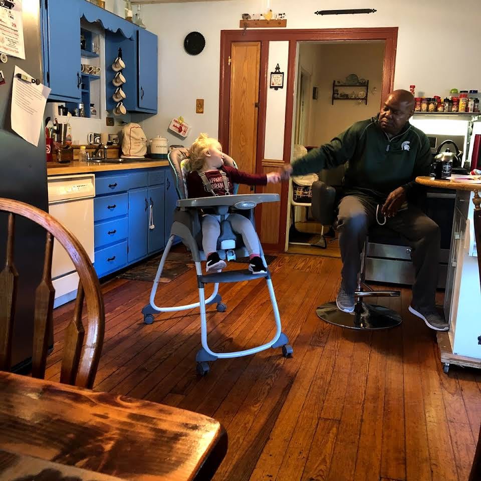 Person and child in high chair reaching for each other in a kitchen