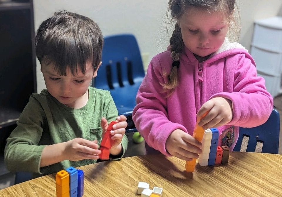 Two children playing with colorful interlocking blocks at a table