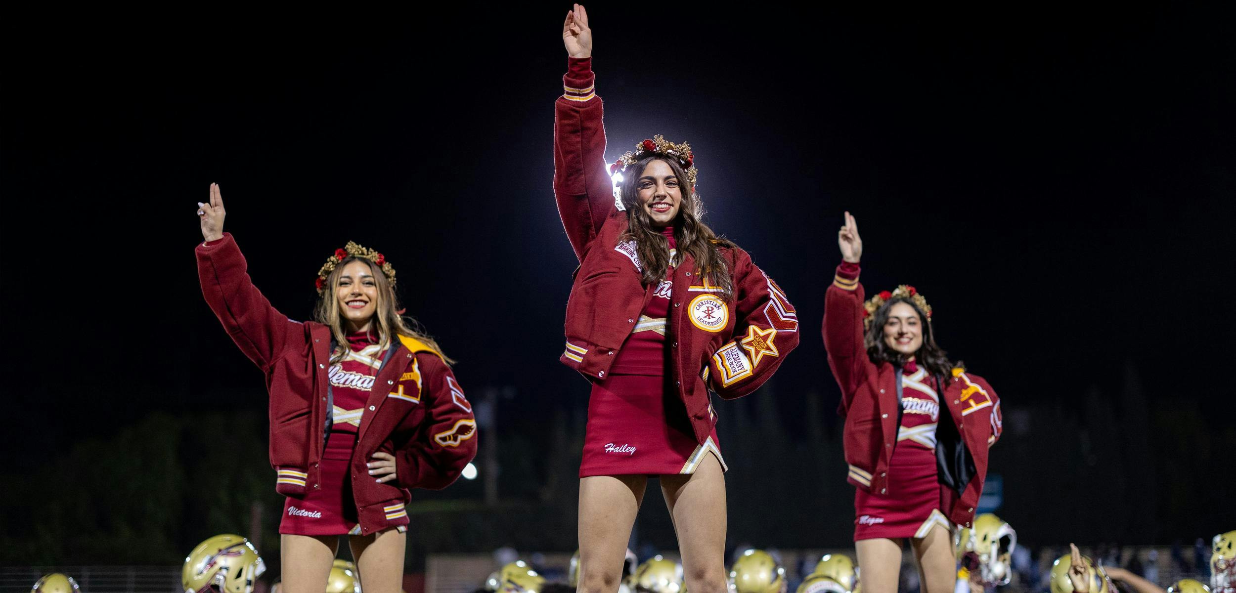 Three people in cheerleading uniforms with letterman jackets raising their hands