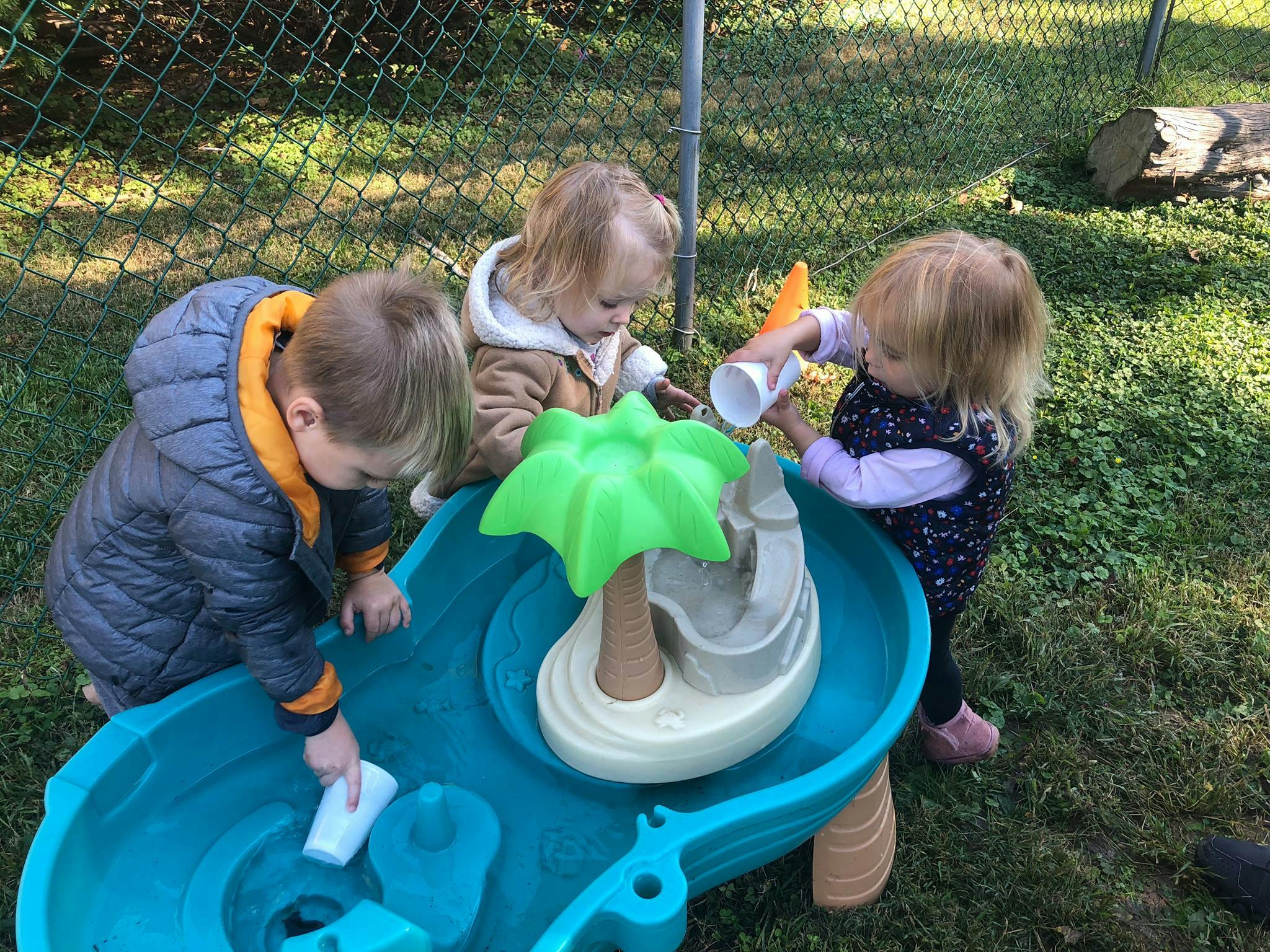 Three children playing with a water table outdoors